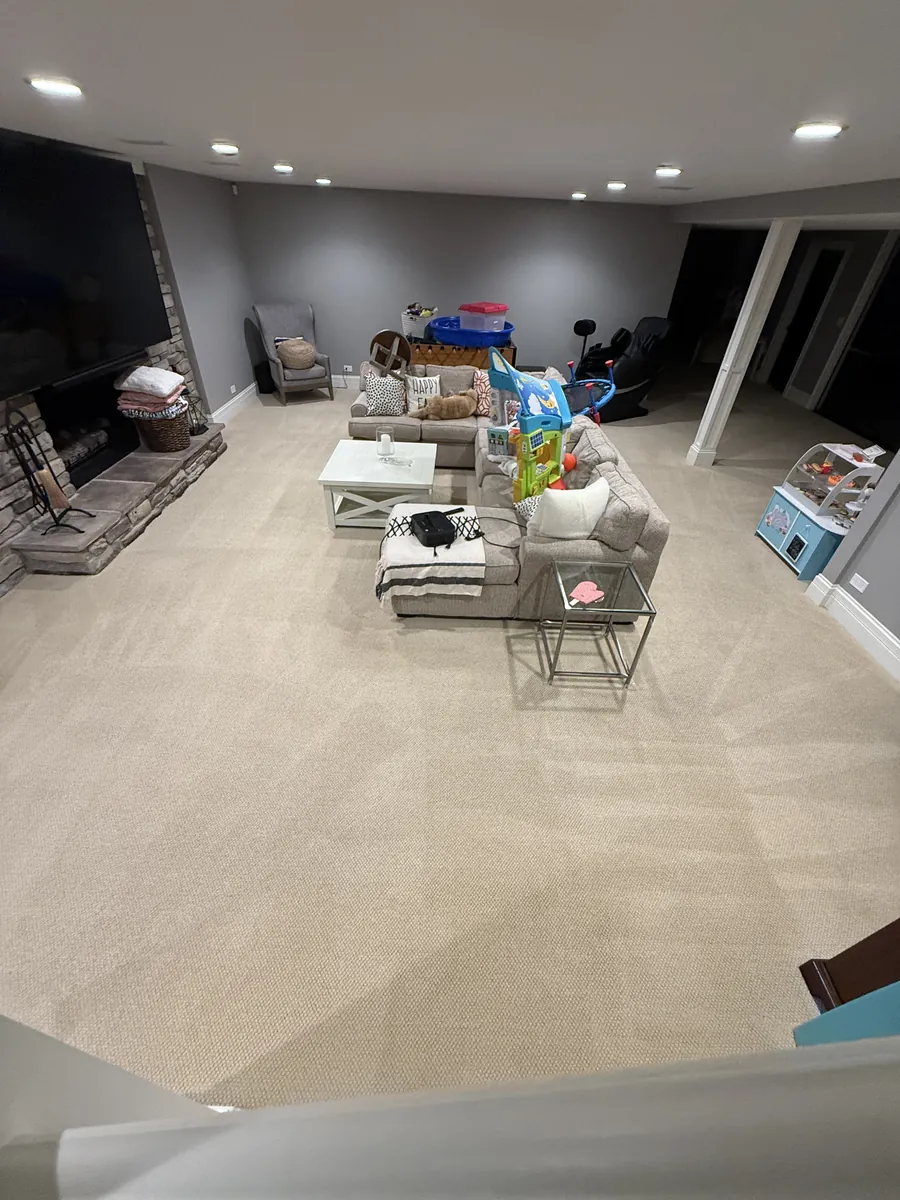 Finished basement family room in Glenview with a stone fireplace, sectional sofa, and freshly cleaned light beige carpet